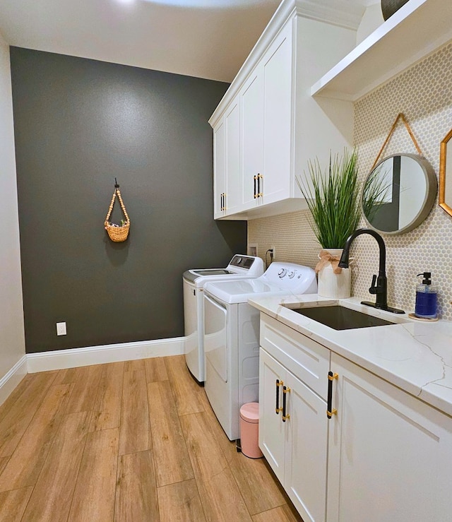 laundry room with washing machine and clothes dryer, cabinet space, a sink, light wood-type flooring, and baseboards