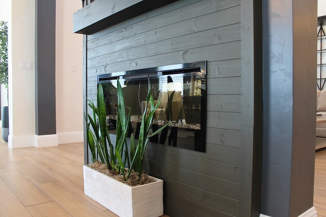 details featuring a glass covered fireplace, wood walls, baseboards, and wood finished floors