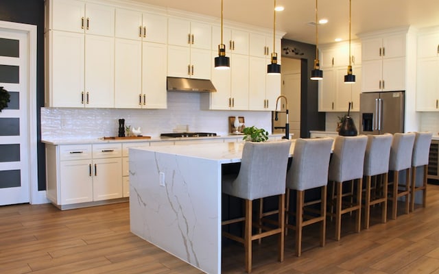 kitchen featuring white cabinets, high quality fridge, light wood-type flooring, under cabinet range hood, and gas cooktop