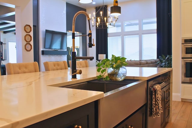 kitchen featuring decorative light fixtures, light stone countertops, an inviting chandelier, stainless steel double oven, and light wood-type flooring