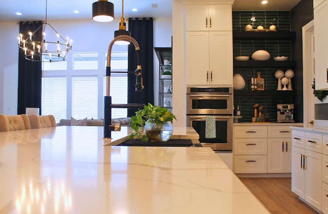 kitchen featuring double oven, light wood-style flooring, white cabinetry, backsplash, and light stone countertops