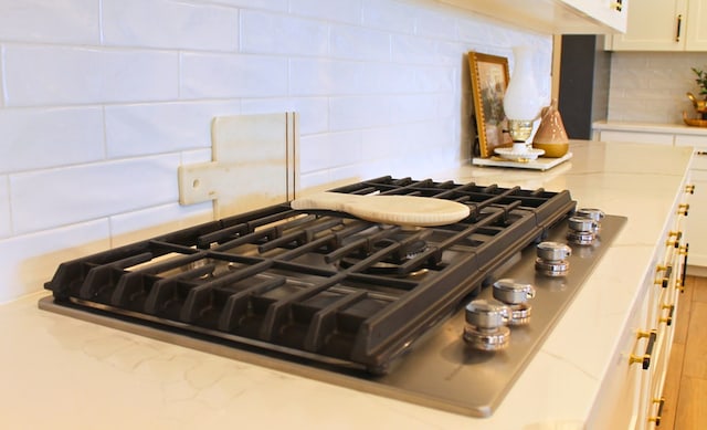 kitchen with tasteful backsplash, light stone countertops, white cabinets, and stainless steel gas stovetop