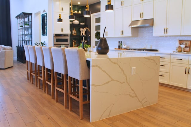 kitchen with gas cooktop, oven, under cabinet range hood, light wood-type flooring, and decorative backsplash