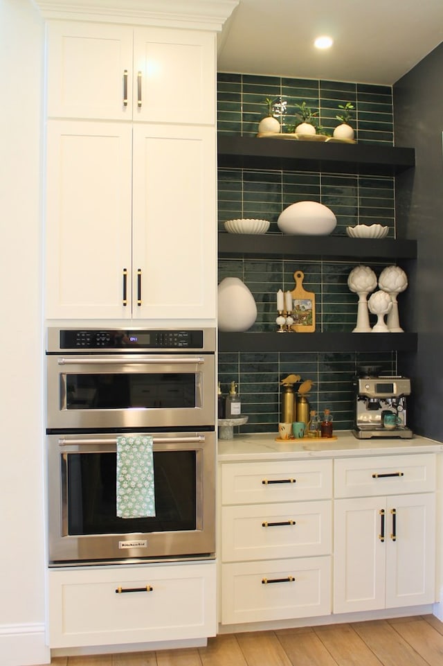 kitchen featuring decorative backsplash, light wood-style flooring, light countertops, double oven, and white cabinetry