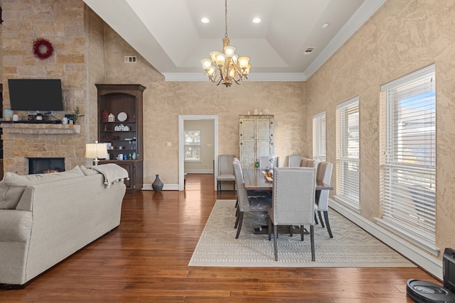 dining room with a notable chandelier, a stone fireplace, dark wood-type flooring, and a tray ceiling