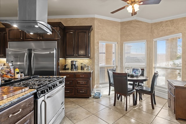 kitchen with high end appliances, light stone counters, island range hood, dark brown cabinets, and ornamental molding