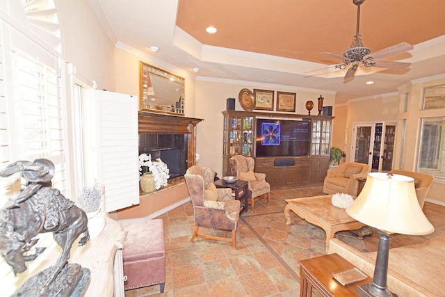 living room with ceiling fan, ornamental molding, a fireplace, and a raised ceiling