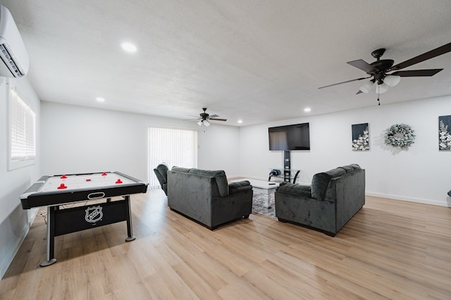 recreation room with a wall mounted air conditioner, ceiling fan, light wood-type flooring, and a textured ceiling