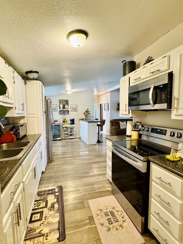 kitchen with white cabinetry, appliances with stainless steel finishes, light wood-style floors, a textured ceiling, and a sink