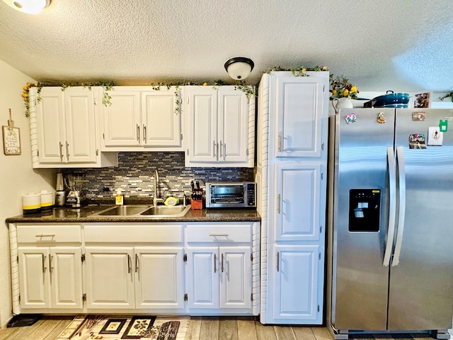 kitchen with dark countertops, backsplash, stainless steel fridge with ice dispenser, light wood-type flooring, and a sink