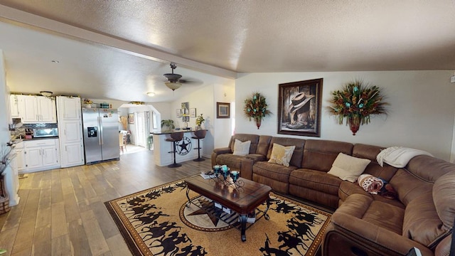 living room with a textured ceiling, ceiling fan, vaulted ceiling with beams, and light wood finished floors