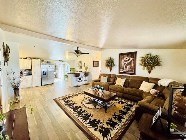 living room with light wood-style floors, ceiling fan, vaulted ceiling with beams, and a textured ceiling