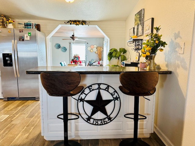 kitchen featuring a breakfast bar area, light wood-type flooring, a peninsula, stainless steel fridge, and a ceiling fan