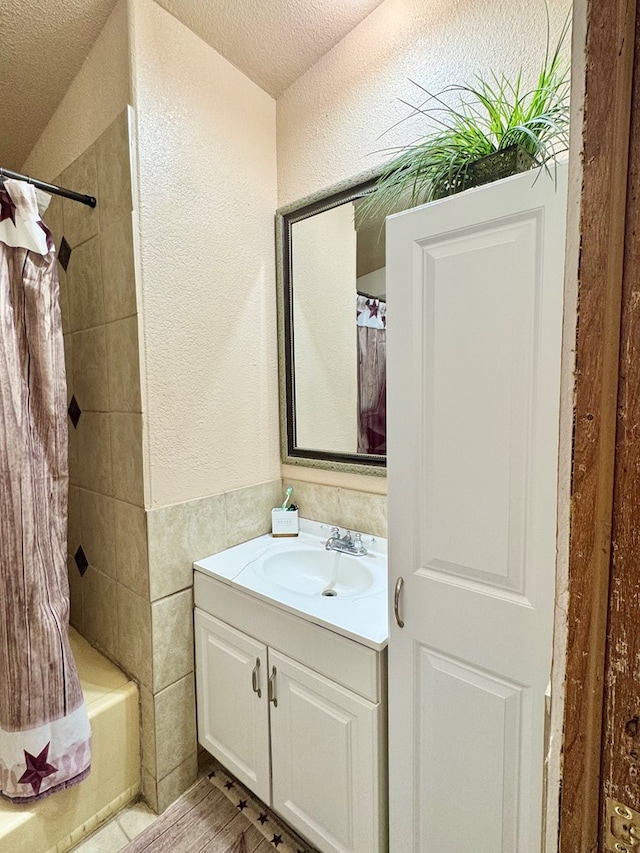 bathroom featuring tile walls, vanity, a textured wall, shower / bath combination with curtain, and a textured ceiling