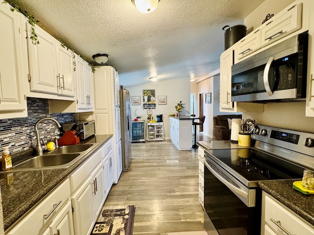 kitchen featuring light wood finished floors, tasteful backsplash, appliances with stainless steel finishes, white cabinetry, and a sink