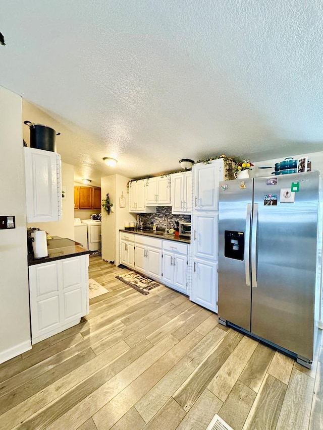 kitchen featuring light wood finished floors, stainless steel fridge with ice dispenser, separate washer and dryer, dark countertops, and backsplash