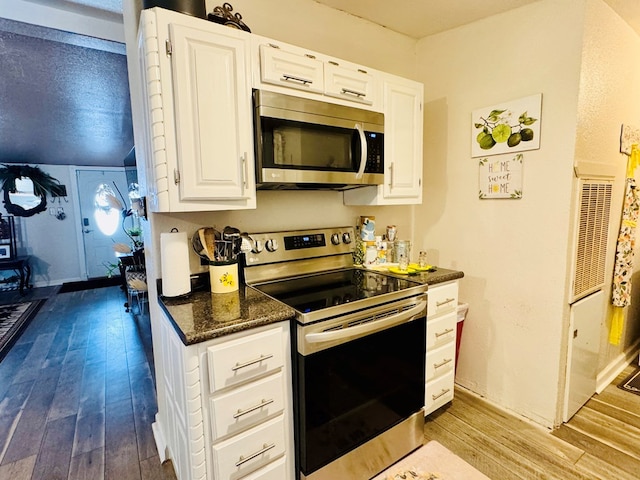 kitchen with dark stone counters, white cabinets, wood-type flooring, and appliances with stainless steel finishes