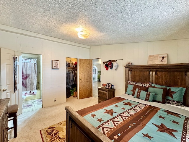 carpeted bedroom featuring a closet, a textured ceiling, a walk in closet, and ensuite bath