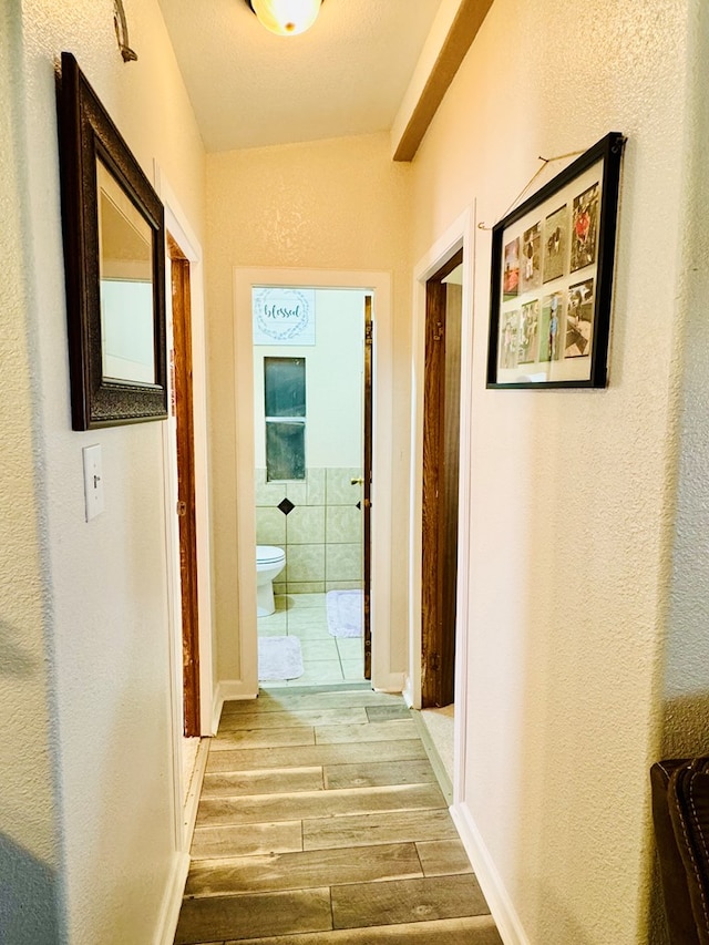 hallway featuring baseboards, wood tiled floor, and a textured wall