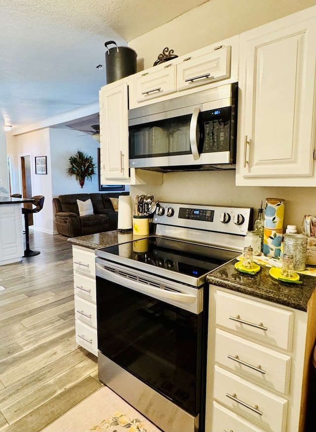 kitchen featuring light wood-type flooring, dark stone countertops, a textured ceiling, white cabinetry, and appliances with stainless steel finishes