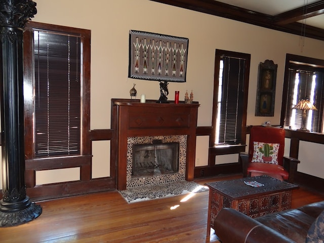 living area with hardwood / wood-style flooring, beam ceiling, crown molding, and a tiled fireplace