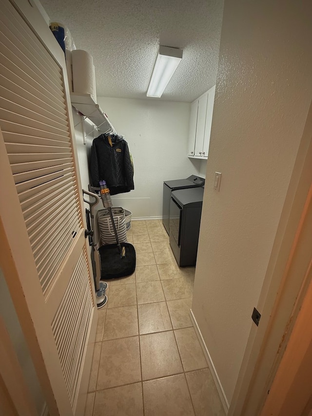 clothes washing area featuring cabinets, washer and dryer, a textured ceiling, and light tile patterned flooring