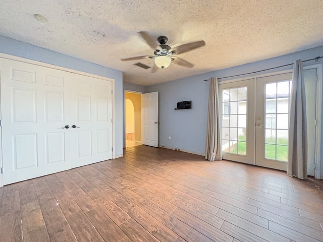 unfurnished bedroom with french doors, a textured ceiling, access to outside, ceiling fan, and hardwood / wood-style flooring