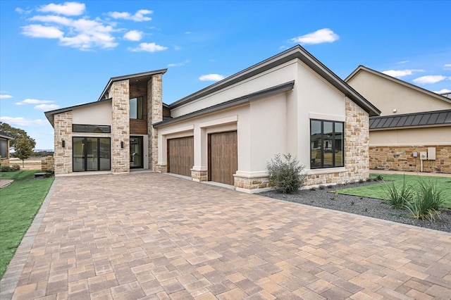 contemporary house featuring a front yard, stucco siding, decorative driveway, a garage, and stone siding