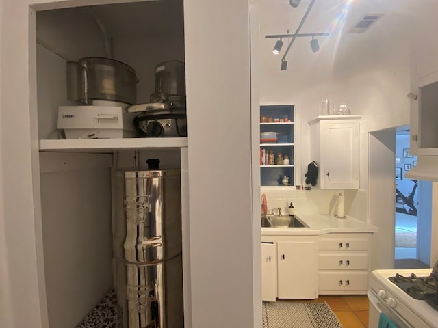 kitchen featuring white cabinets, light tile patterned floors, white gas range oven, and sink