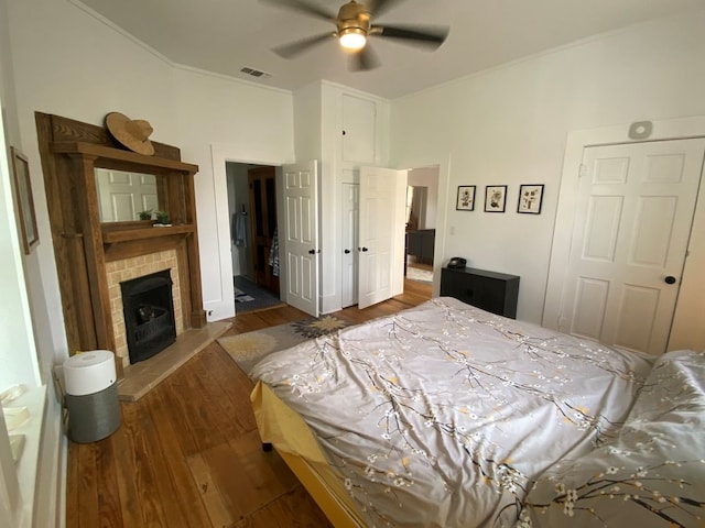 bedroom with ceiling fan, dark hardwood / wood-style flooring, crown molding, and a tile fireplace