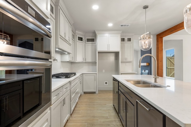 kitchen with sink, appliances with stainless steel finishes, white cabinetry, hanging light fixtures, and light stone counters