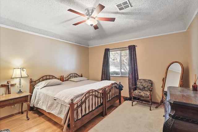 bedroom featuring a textured ceiling, a ceiling fan, visible vents, light wood finished floors, and crown molding