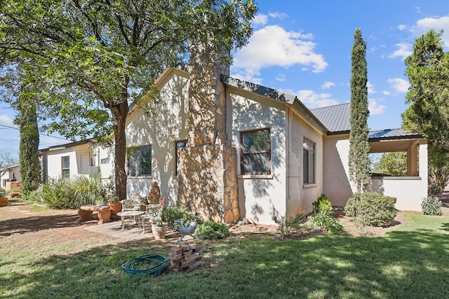 rear view of house featuring metal roof, a yard, a patio area, and stucco siding