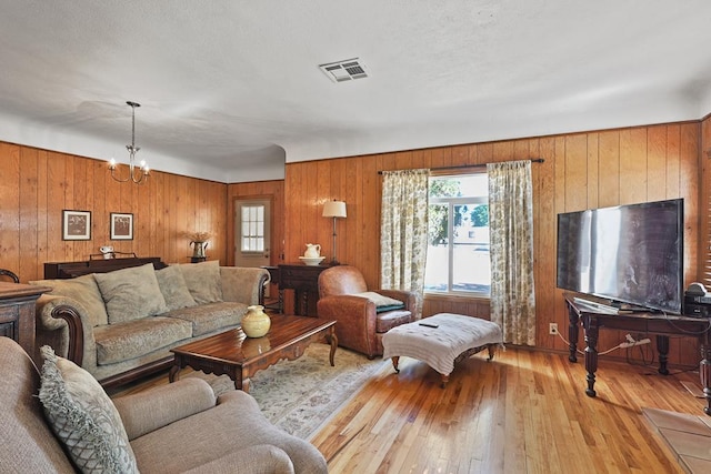 living area with light wood-type flooring, visible vents, a notable chandelier, and wooden walls