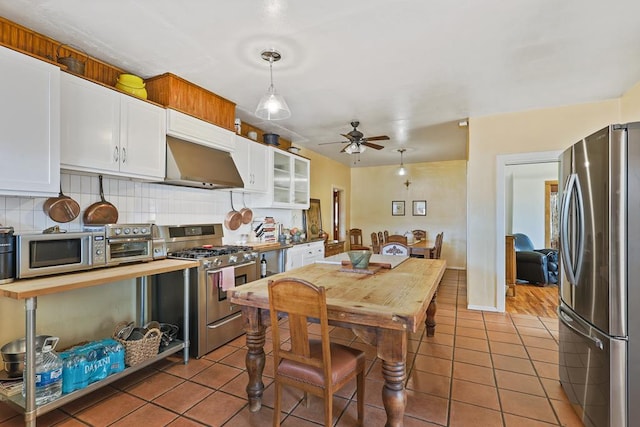 kitchen with backsplash, appliances with stainless steel finishes, white cabinets, tile patterned flooring, and under cabinet range hood