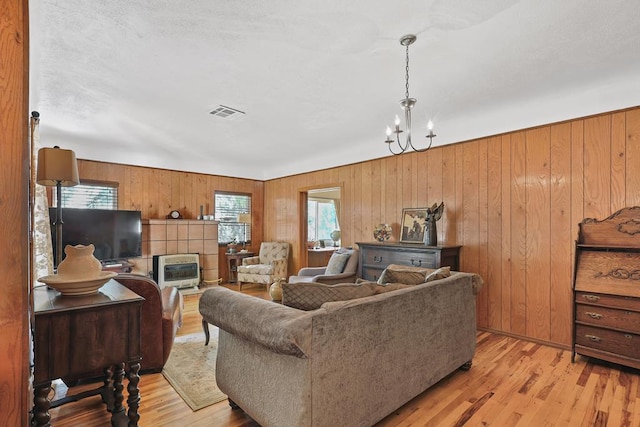 living room featuring visible vents, wooden walls, light wood-style flooring, and a notable chandelier