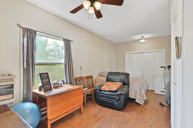 bedroom featuring a closet, ceiling fan, heating unit, and wood finished floors