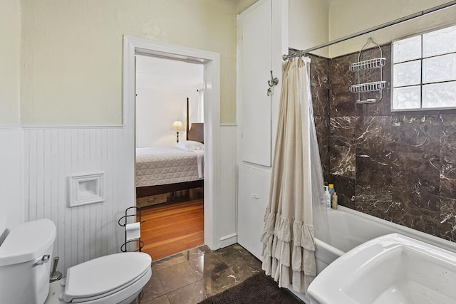 ensuite bathroom featuring a wainscoted wall, shower / bath combination with curtain, toilet, and connected bathroom