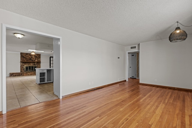 spare room featuring a stone fireplace, a textured ceiling, and light wood-type flooring