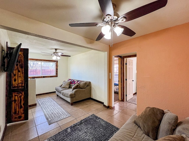 living area featuring light tile patterned floors, a ceiling fan, and baseboards