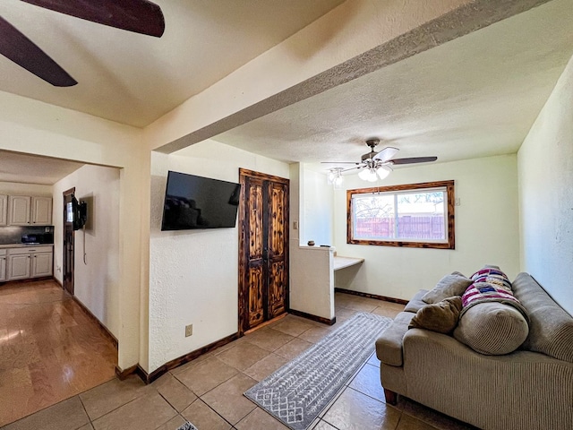 living room featuring light tile patterned floors, baseboards, ceiling fan, a textured ceiling, and a textured wall