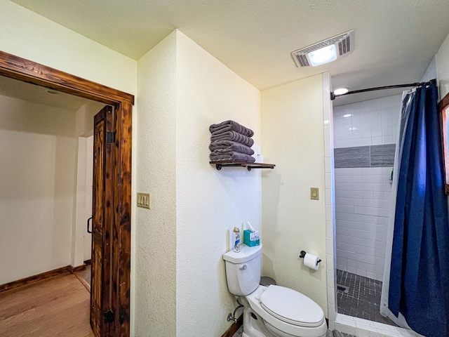 bathroom featuring visible vents, baseboards, toilet, tiled shower, and wood finished floors