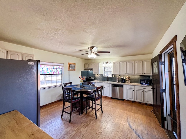 kitchen with a sink, backsplash, stainless steel appliances, light wood-style floors, and ceiling fan