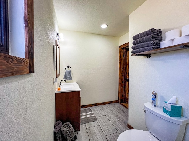 bathroom with toilet, wood tiled floor, baseboards, vanity, and a textured wall