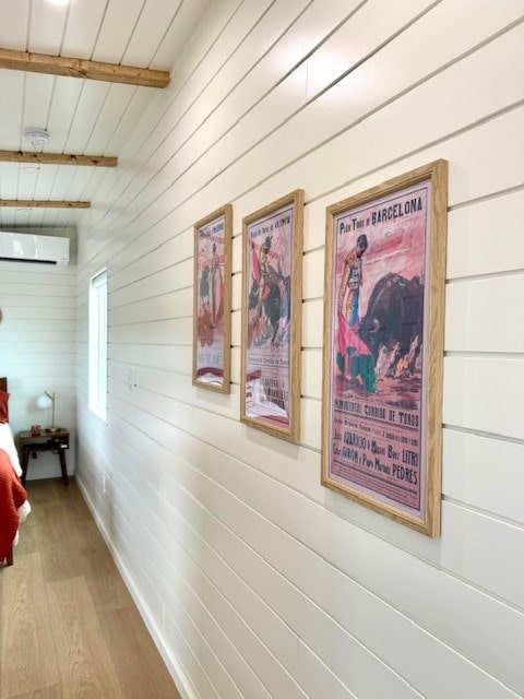 corridor featuring wooden walls, wood finished floors, baseboards, beam ceiling, and a wall mounted air conditioner