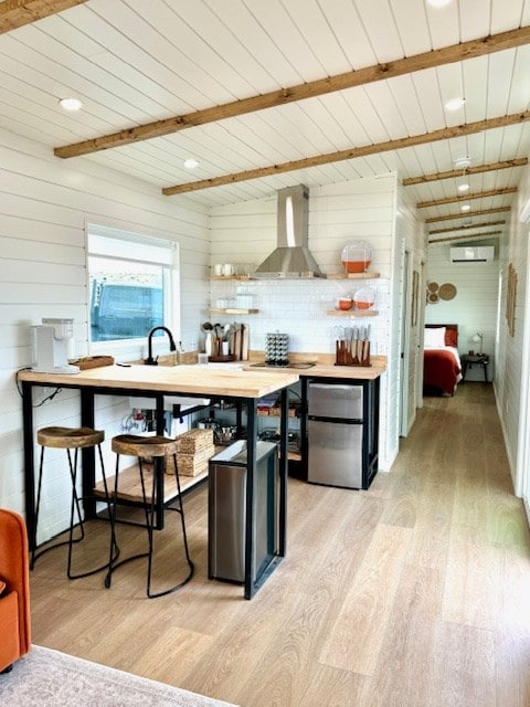 kitchen with electric cooktop, light wood-style floors, freestanding refrigerator, wall chimney exhaust hood, and a wall mounted air conditioner