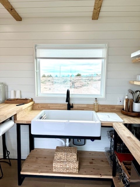 kitchen with wood finished floors, beamed ceiling, a sink, and wooden walls