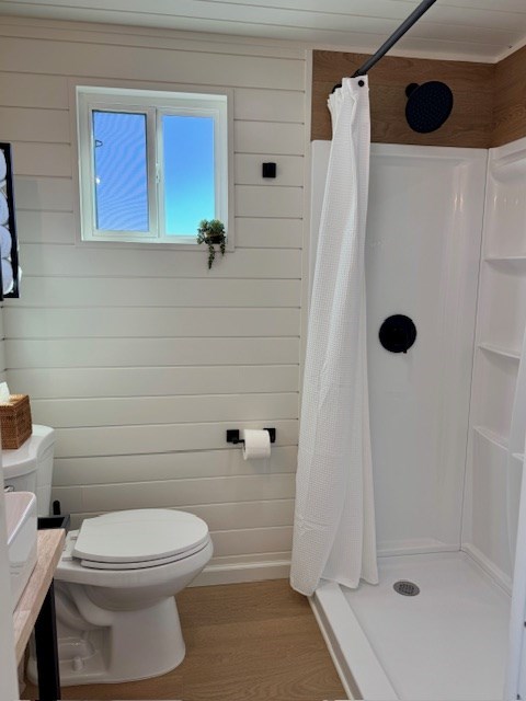 bathroom featuring wood finished floors, a shower stall, toilet, and wooden walls