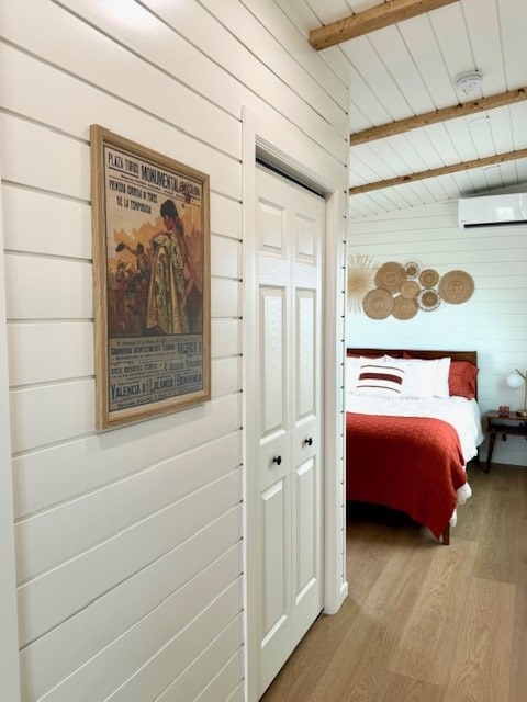 bedroom featuring a closet, a wall unit AC, wood finished floors, and wooden walls