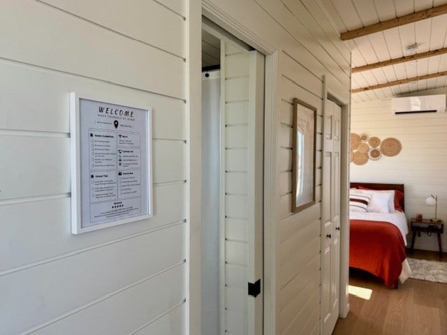 corridor with wooden walls, wooden ceiling, wood finished floors, a wall mounted air conditioner, and beam ceiling